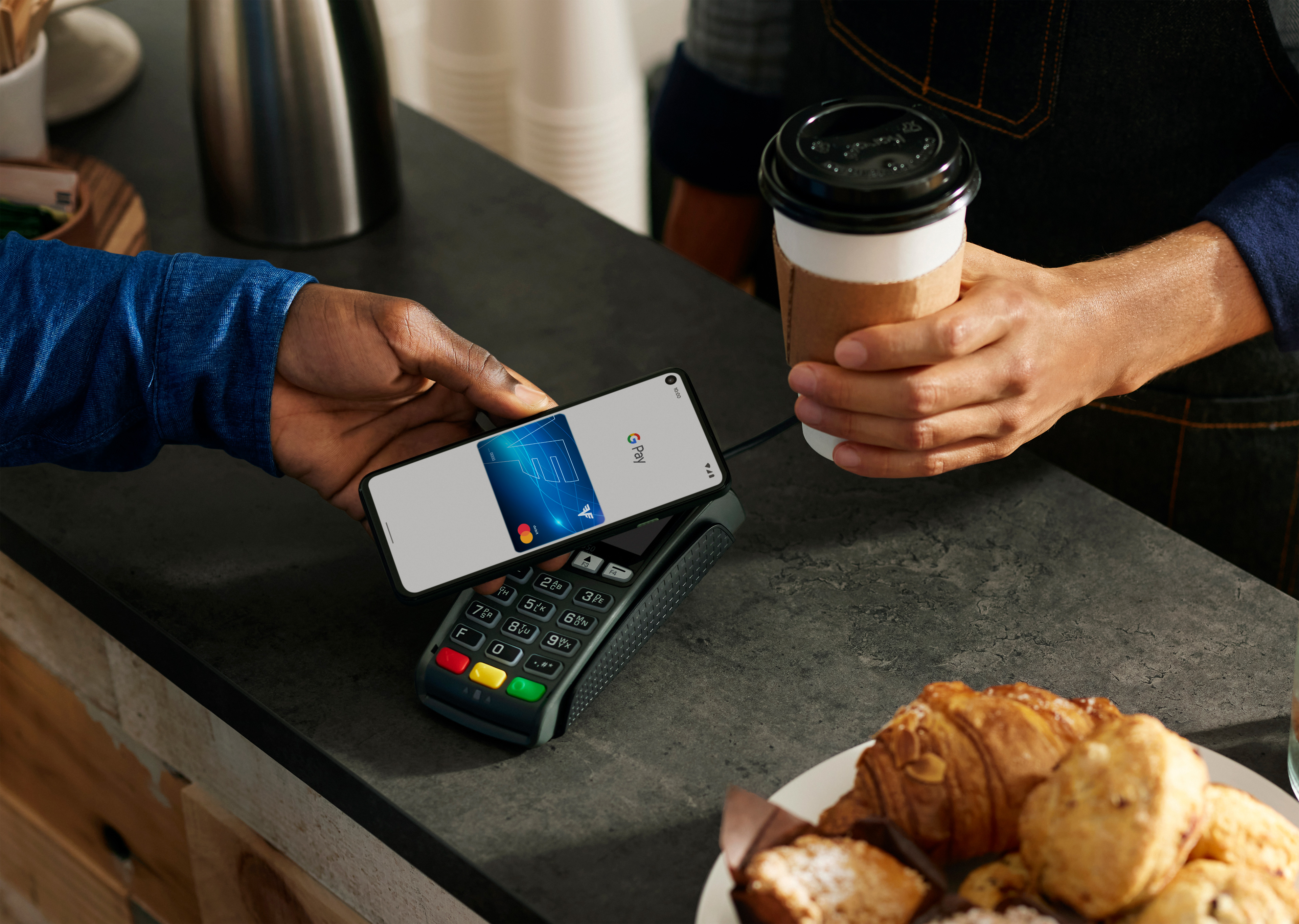 Ein Mann zahlt mit Smartphone Google Pay und Volksbank Mastercard in einem Café.