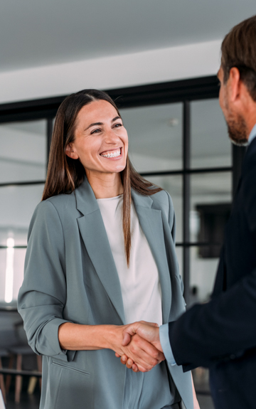 Eine glückliche Frau im Blazer schüttelt jemandem die Hand im Büro.